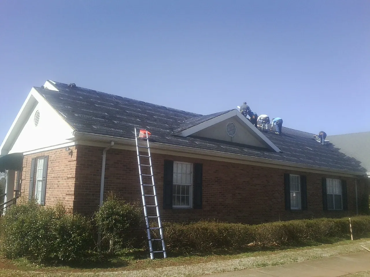 Crew tearing shingles off a brick ranch roof with a ladder set — Emergency Roof Repair work by our crew in Kenner
