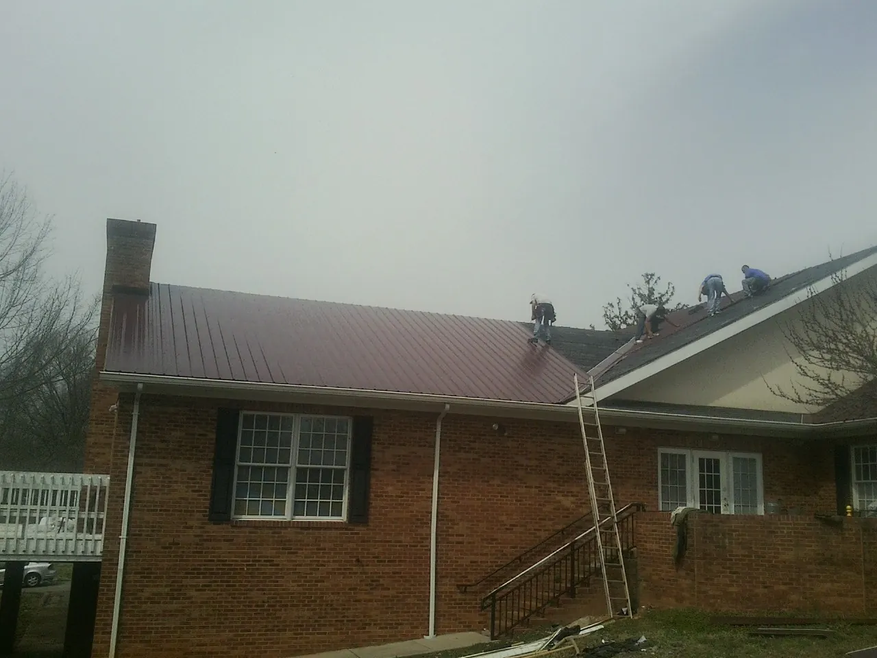 Crew setting red metal roofing panels on a brick home in Kenner