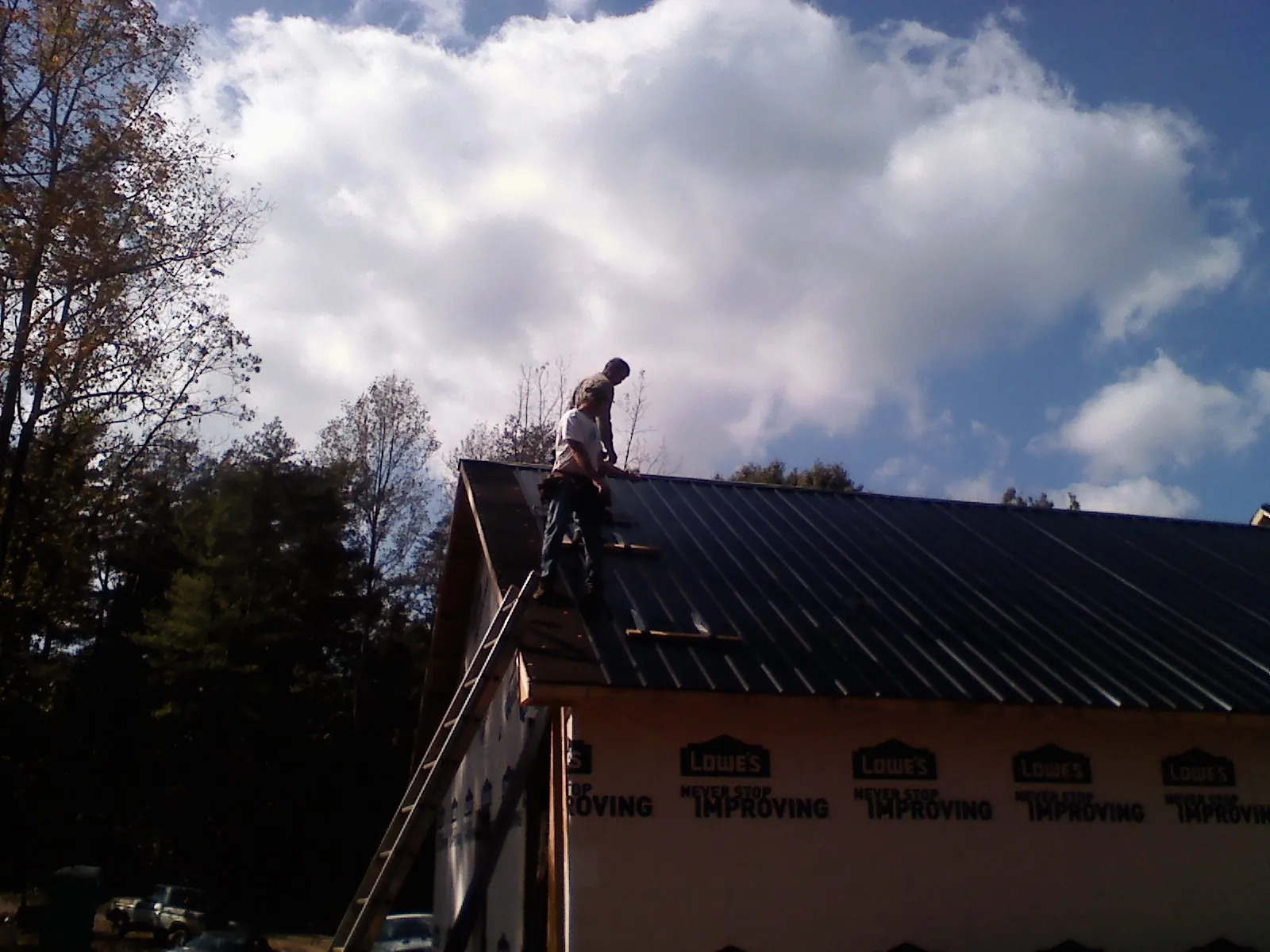 Roofer fastening dark metal panels high against a cloudy sky, from a Roof Inspection job in Kenner