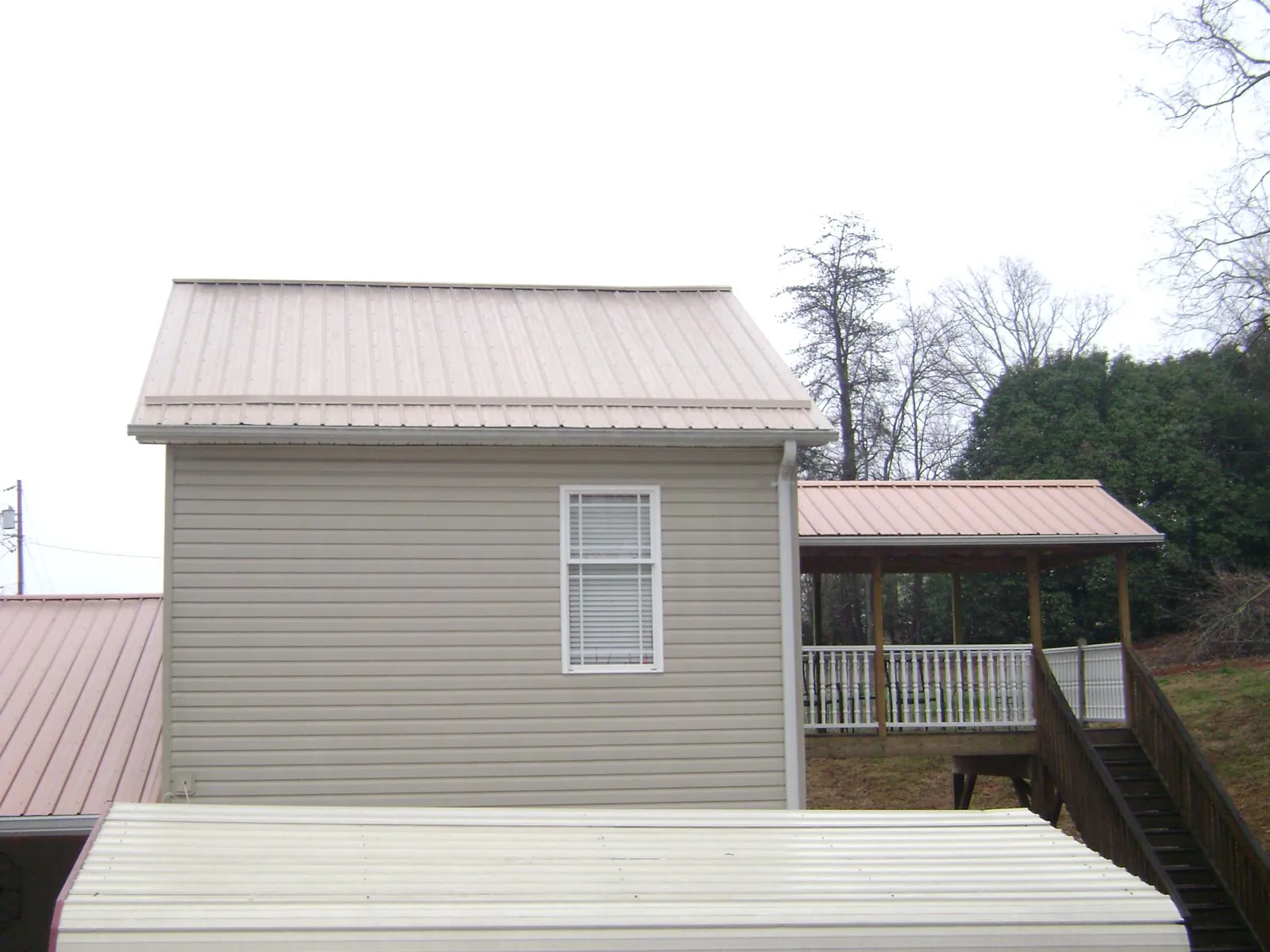 Tan metal roofs on a two story addition and attached porch, from a Roof Replacement job in Kenner